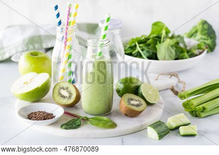 A Bottle Of Green Smoothie Surrounded By Ingredients Used To Make It.