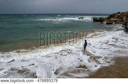 Drone Aerial Of Young Boy In Shorts Standing On The Summer Beach And Looking At The Stormy Spindrift