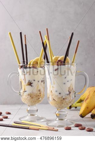 Two Glasses Of Granola With Chocolate And Banana, Decorated With Sticks Pocky
