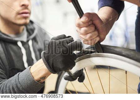 Two Men Working Together Collaboratively To Remove An Airless Tire From A Bicycle Wheel At A Bike Re