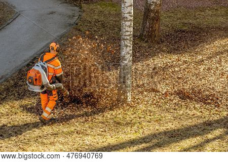 City Leaf Cleaner Blowing Up Fallen Leaves On Sunny Early Spring Day. Service Worker Operating Backp