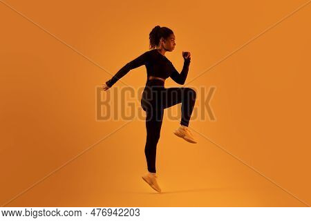 Fitness Studio Dedication. Determined Black Woman Jumping And Doing Elbow To Knee Crunch Over Orange