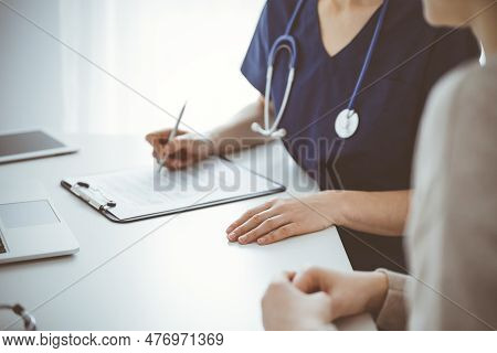 Doctor And Patient Sitting At The Table In Clinic While Discussing Something. The Focus Is On Female