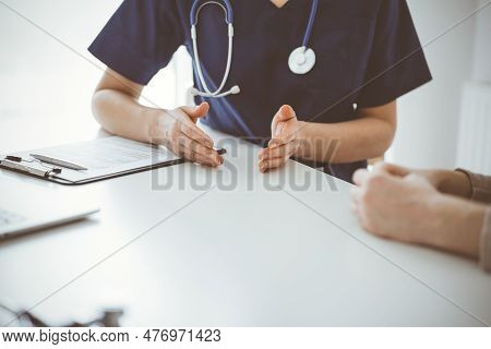 Doctor And Patient Sitting At The Table In Clinic While Discussing Something. The Focus Is On Female