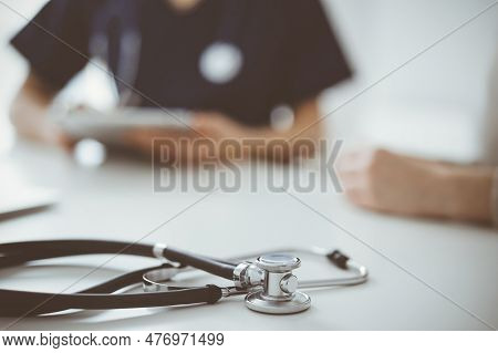 Stethoscope Lying On The Tablet Computer In Front Of A Doctor And Patient At The Background. Medicin
