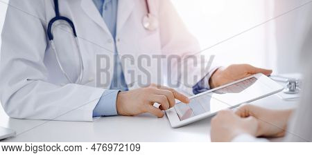Doctor And Patient Sitting Opposite Each Other At The Desk In Clinic. The Focus Is On Female Physici