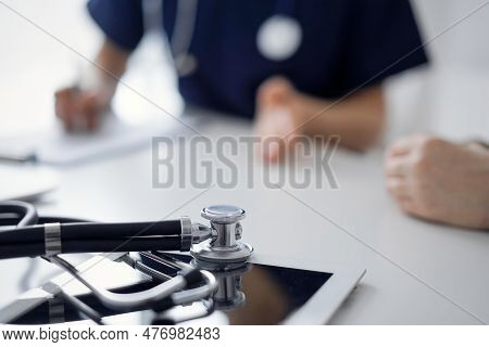 Stethoscope Lying On The Tablet Computer In Front Of A Doctor And Patient At The Background. Medicin