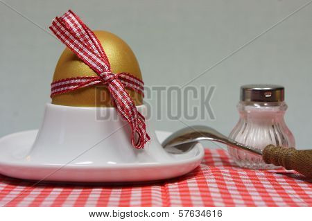 Golden Egg In An Egg Cup On A Red Patterned Napkin