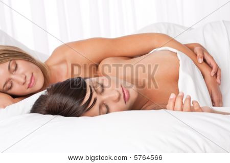 Két fiatal nő fehér ágyban fekve