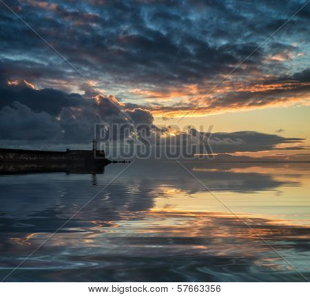 Beautiful Vibrant Sunrise Sky Over Calm Water Ocean With Lighthouse And Harbor Wall