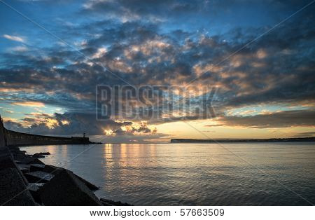 Beautiful Vibrant Sunrise Sky Over Calm Water Ocean With Lighthouse And Harbor Wall