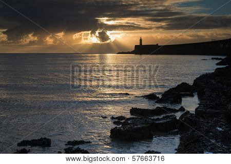 Beautiful Vibrant Sunrise Sky Over Calm Water Ocean With Lighthouse And Harbor Wall