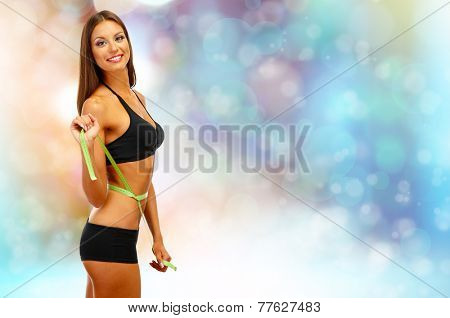 Beautiful young woman with measuring tape on bright background