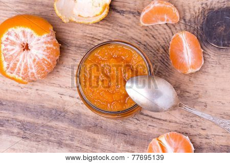 Colorful homemade tangerine jam in glass jar on rustic wooden board