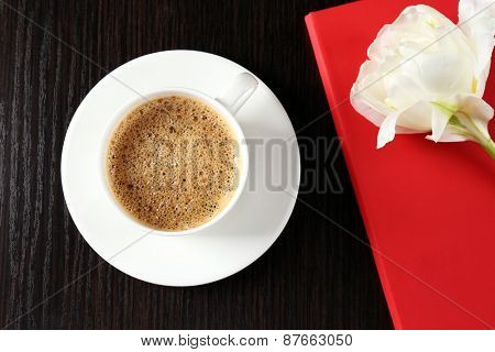 Cup of coffee with notebook and fresh flower on wooden table background