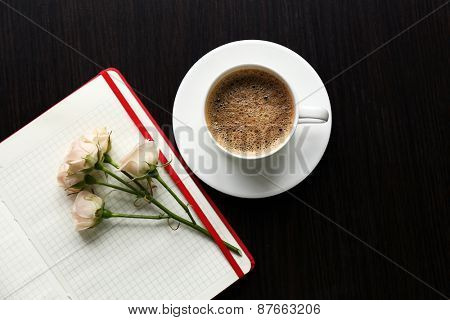 Cup of coffee with notebook and fresh flower on wooden table background