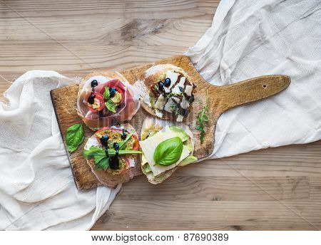Antipasti Brusquetta Set On A Rustic Wooden Board Over A Linen Kitchen Towel And Wooden Surface