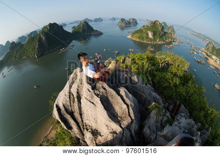 A young traveler man sit on the top of mountain with his guitar in Halong bay and enjoy the beauty of seascape.