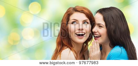 friendship, secrecy and people concept - two smiling girls or young women whispering gossip over green lights background