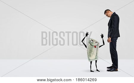 A businessman looking down at a humanoid dollar bill that makes faces. Loss of credit. Laughable sum. Banking for small companies.