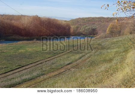 A picturesque autumn road against the background of hills, forests and the river.