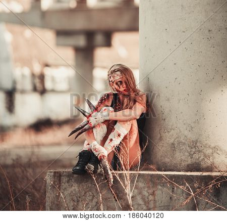 Mutant girl in wounds and ulcers with claws instead of fingers. She is sitting.