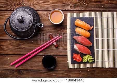 Sushi Set served on gray stone slate with soy sauce, grey teapot and cup of tea on wooden background