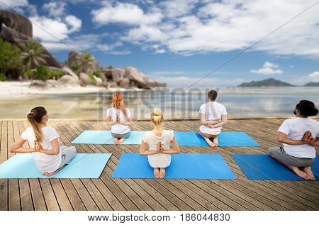 fitness, yoga, meditation and sport concept - group of people exercising in reverse prayer pose over exotic tropical beach background