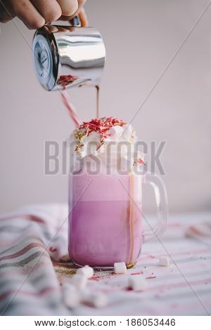 Woman is pouring coffee in stylized mason jar cup of colored milk with cream marshmallow and colorful decoration. Milk shake cocktaill frappuccino. Unicorn coffee unicorn food.