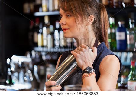 alcohol drinks, people and luxury concept - barmaid with shaker preparing cocktail at bar