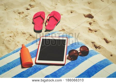 Vacation accesssories - suncream, flip-flops and touch pad on beach