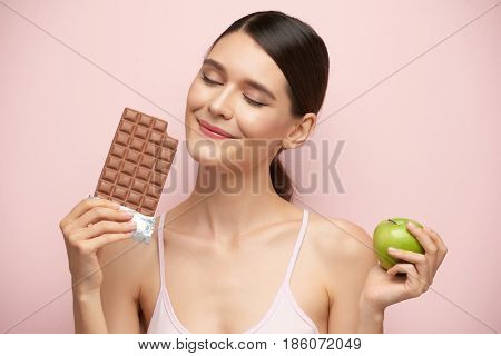 Smling young woman preferring milk chocolate to apple