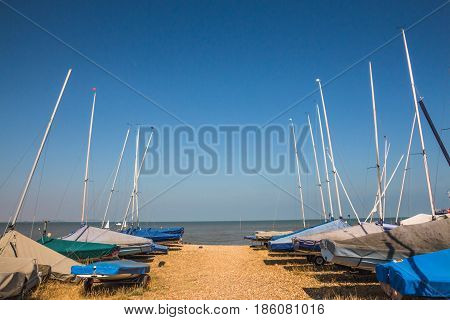 Small sailing boats lined up near the sea on the sand at Whitstable Kent United kingdom