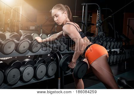 Attractive fit woman working out with dumbbells as a fitness conceptual image over dark gym background.