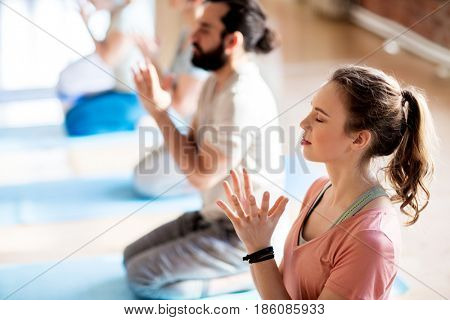 fitness, yoga and healthy lifestyle concept - group of people doing lotus seal gesture and meditating in seated pose at studio