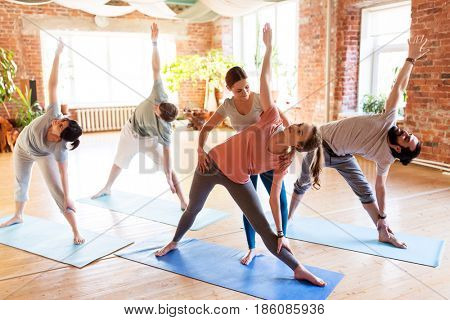fitness, sport and healthy lifestyle concept - group of people with personal trainer doing yoga exercises on mats in gym or studio