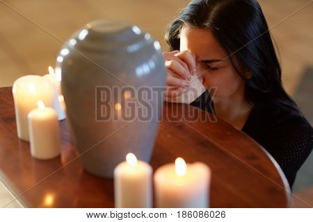 burial, people and mourning concept - sad woman with cinerary urn and candles praying at funeral in church