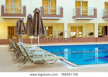 Empty sunbeds and umbrellas are at pool empty without tourists early in morning. Relax and sunbathe by pool with clear blue water in Resort hotel. Bali Rethymno Crete Greece
