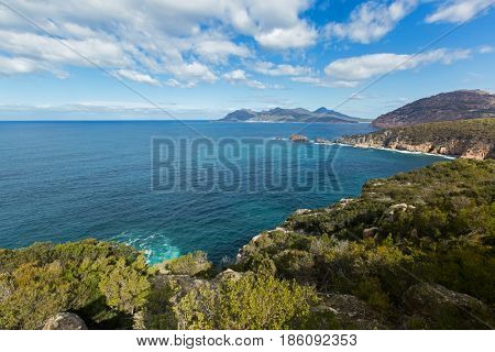 Turquoise waters of Carp bay, view from Cape Tourville Lighthouse lookout - Seascape photo, cliff coastline, green mountain, blue sky at Freycinet National Park, Tasmania, Australia 