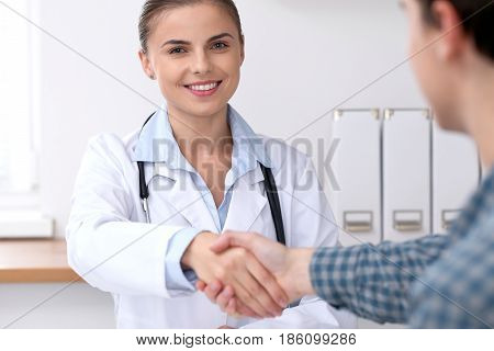 Doctor woman smiling while shaking hands with her male patient. Medicine and trust concept.
