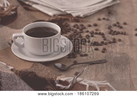 A cup of black coffee on a wooden table with grains and newspaper a gray toning. Black Coffee Grain Newspaper Wooden Background Retro Photo Breakfast