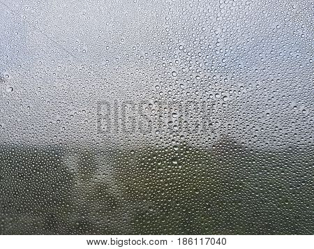 Rain drops on the window see blurry thru the park and the dark cloudy sky behind. selective focus lens blur