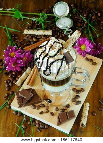 Coffee cocktail with whipped cream in an Irish coffee mug surrounded by coffee beans, cinnamon and chocolate bars