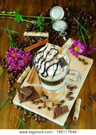 Coffee cocktail with whipped cream in an Irish coffee mug surrounded by coffee beans, cinnamon and chocolate bars