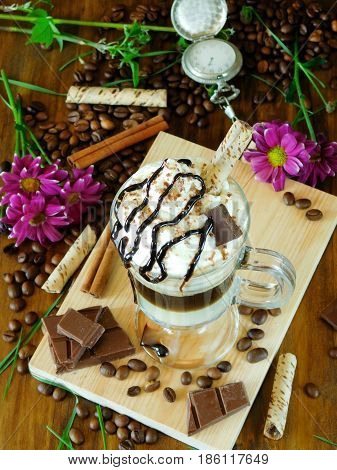 Coffee cocktail with whipped cream in an Irish coffee mug surrounded by coffee beans, cinnamon and chocolate bars