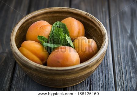 Ripe orange apricots in a clay bowl on a wooden table