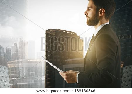 Side view of young businessman holding documet on sunlit city background. Business concept
