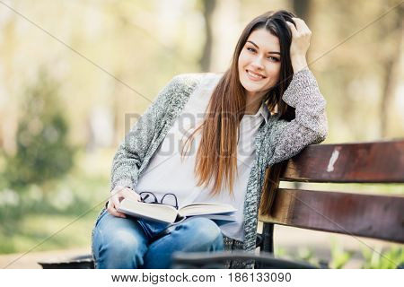 Beautiful University Student Reading At The Park On Bench