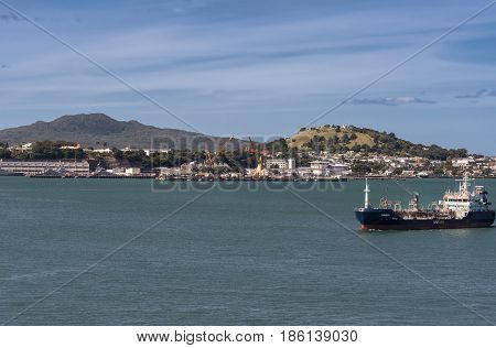 Auckland New Zealand - March 6 2017: Tanker sails in harbor in front of Devonport city under blue sky on green water. Rangitoto and Victoria volcanoes in background.