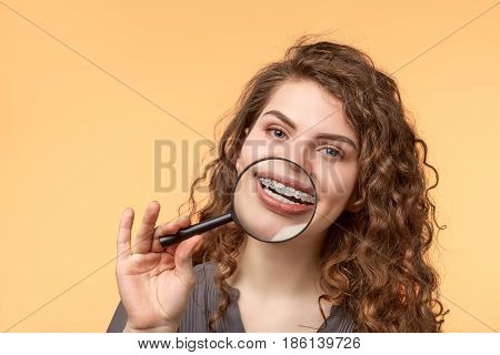 curly hair woman with brackets on biege background with magnifier